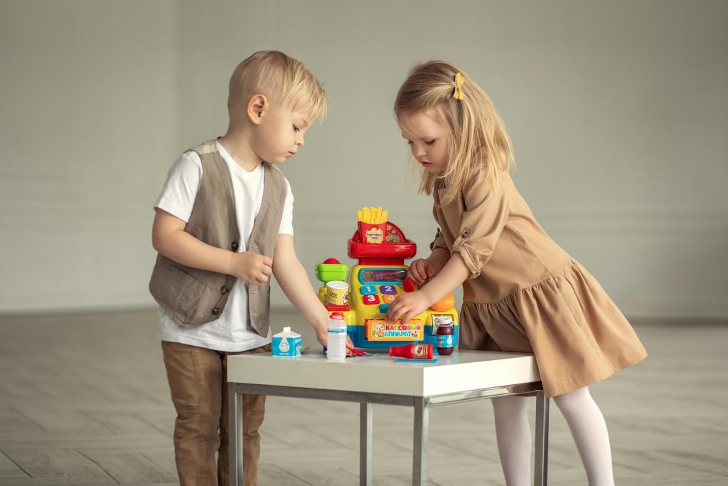 Two children engaging with a toy cash register at a table, capturing playful innocence.