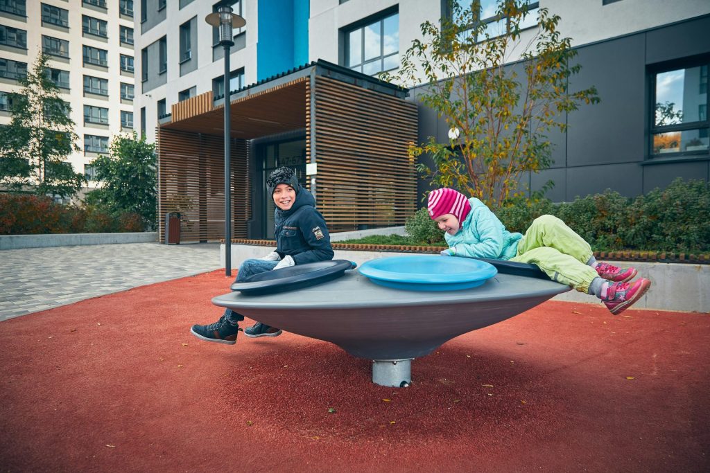 Two children joyfully playing on a modern playground near an apartment building on a clear day.