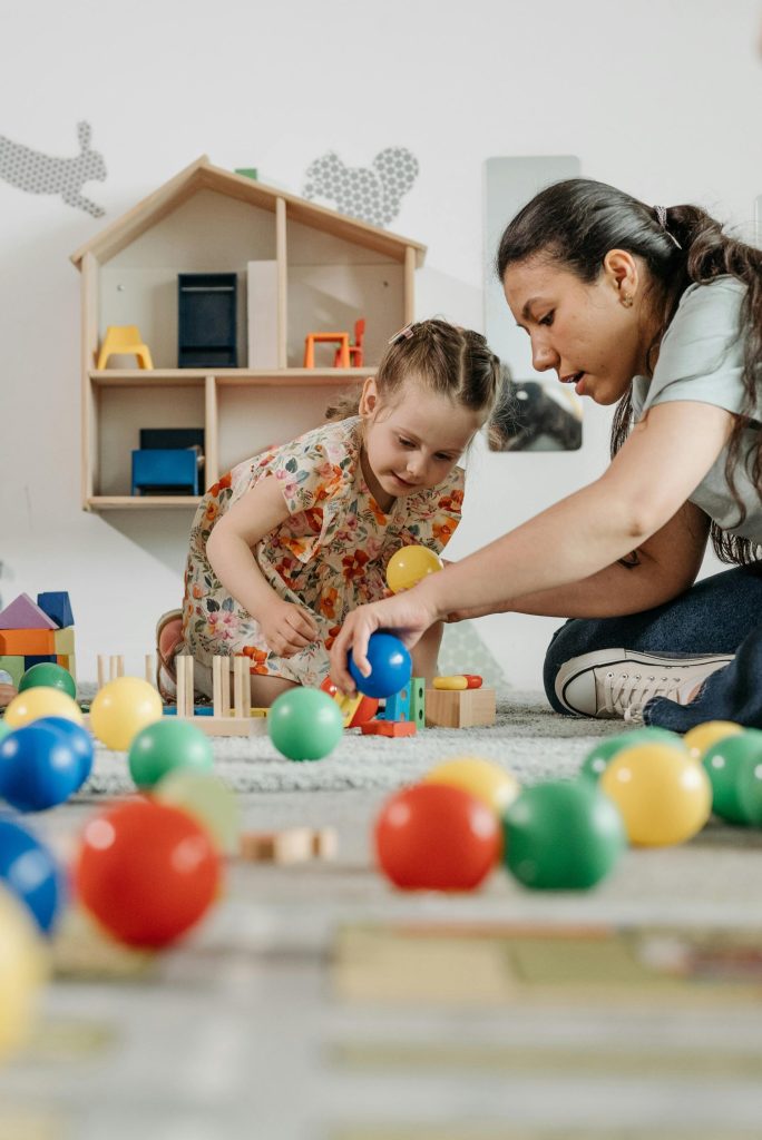 A woman and a child playing with colorful balls and blocks in a kindergarten setting.